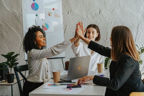 Équipe féminine composée de trois femmes, se tapant la main pour illustrer une réussite. L'agence JVFlex utilise cette photo afin d'imager l'offre de création de site internet sur mesure. Site plus léger et mieux référencés grâce au SEO